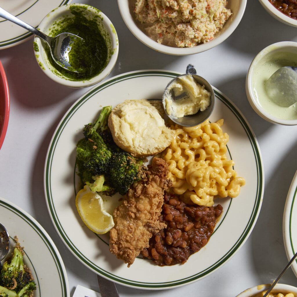 a white table set with lots of plates and bowls. The plate in the center has fried chicken, mac n cheese, beans, a biscuit