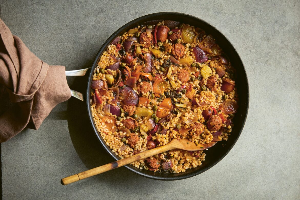 dirty rice in a cast iron pan with a wooden spoon with a brown tea towel wrapped around the pan handle