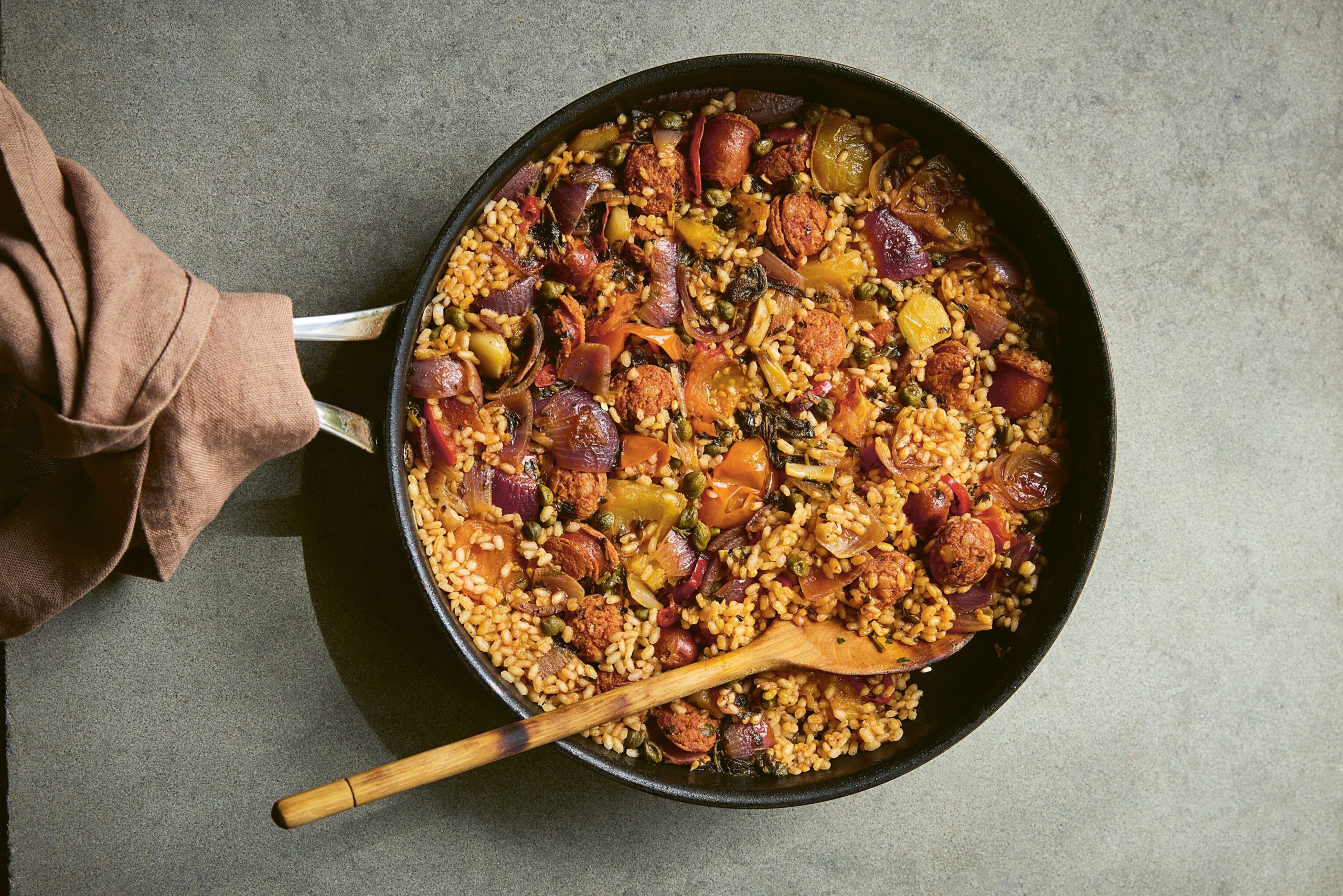 dirty rice in a cast iron pan with a wooden spoon with a brown tea towel wrapped around the pan handle